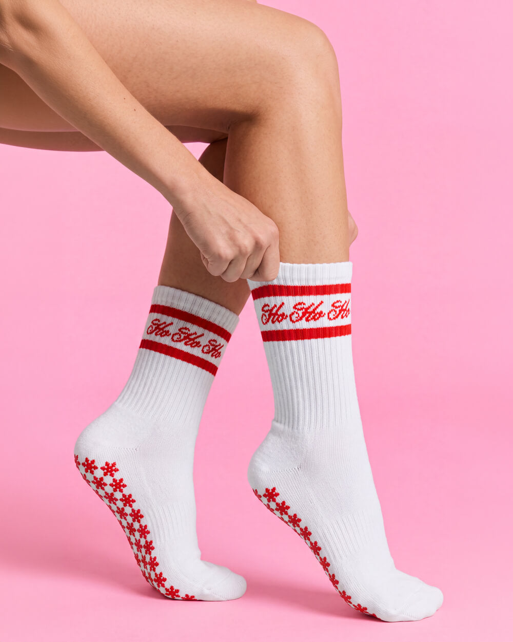 Ho Ho Ho Christmas grip socks worn on crossed legs against a pink background