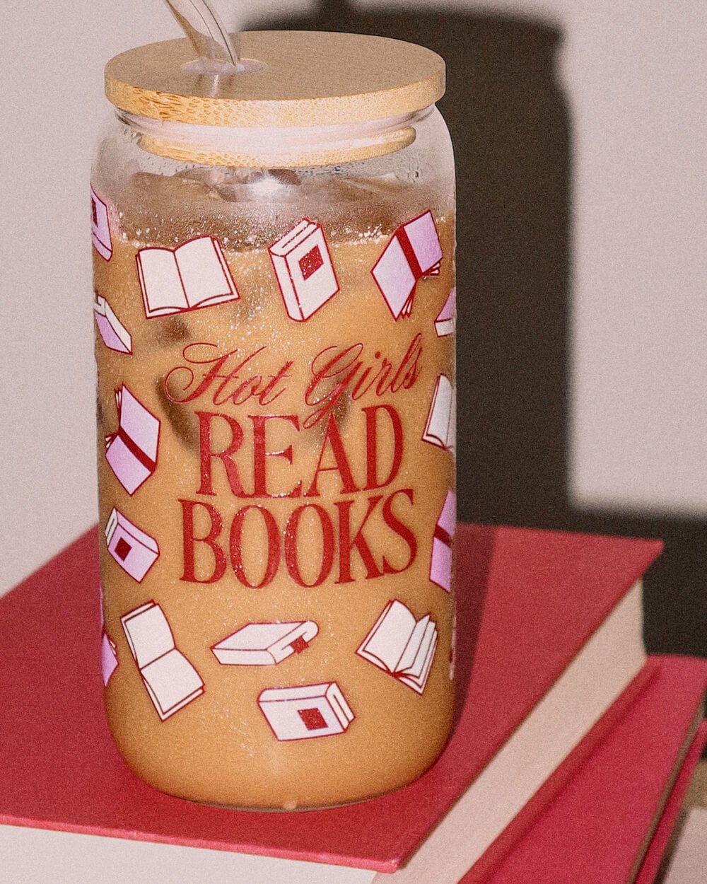 Hot Girls Read Books tumbler of iced coffee resting on a stack of red hardcover books