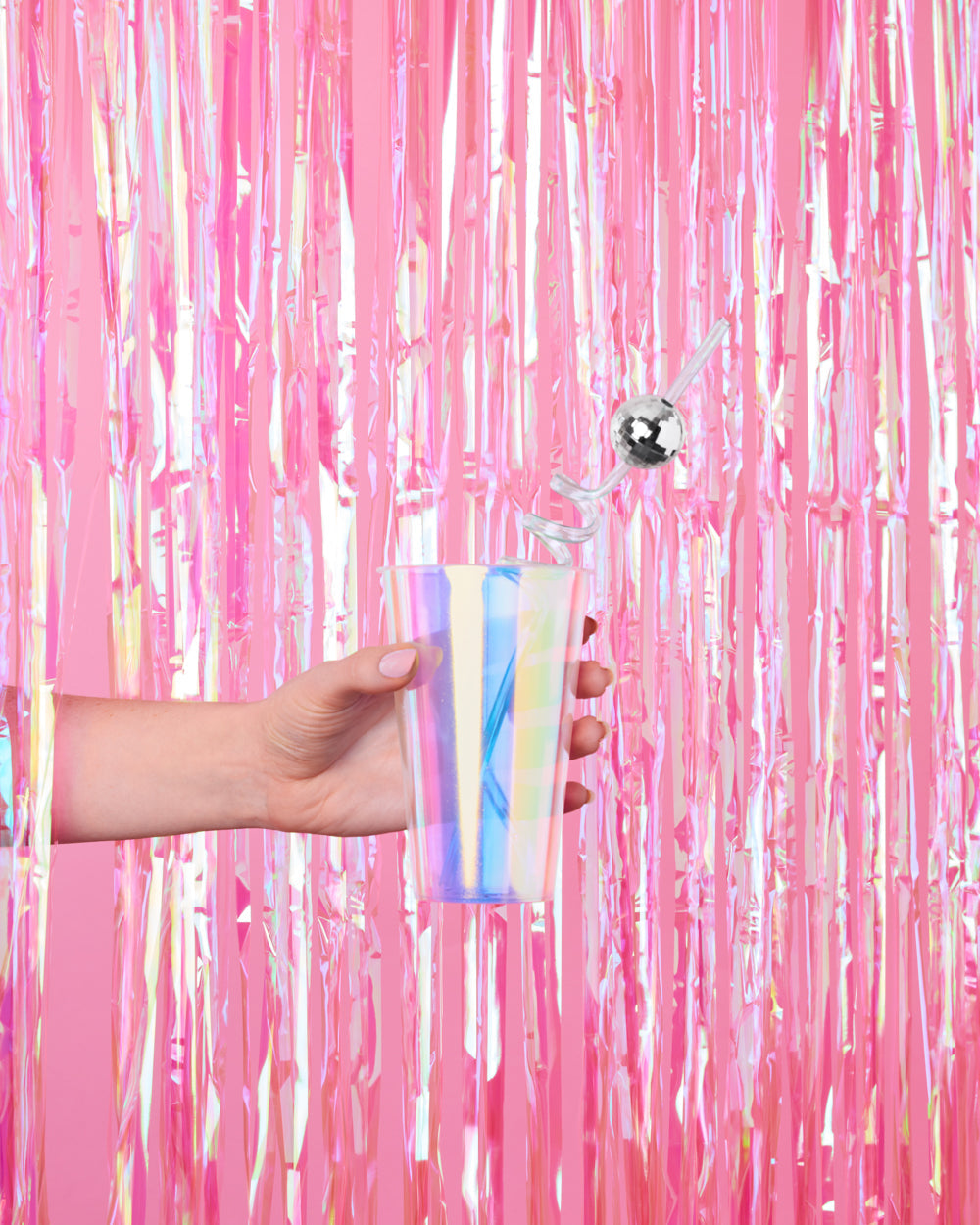 Hand holding an iridescent cup in front of a hot pink fringe curtain party backdrop