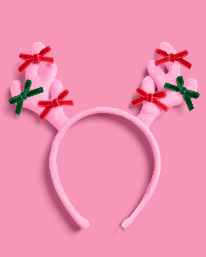 Pink reindeer antlers headband in plush velvet with red and green bows on each antler, on pink