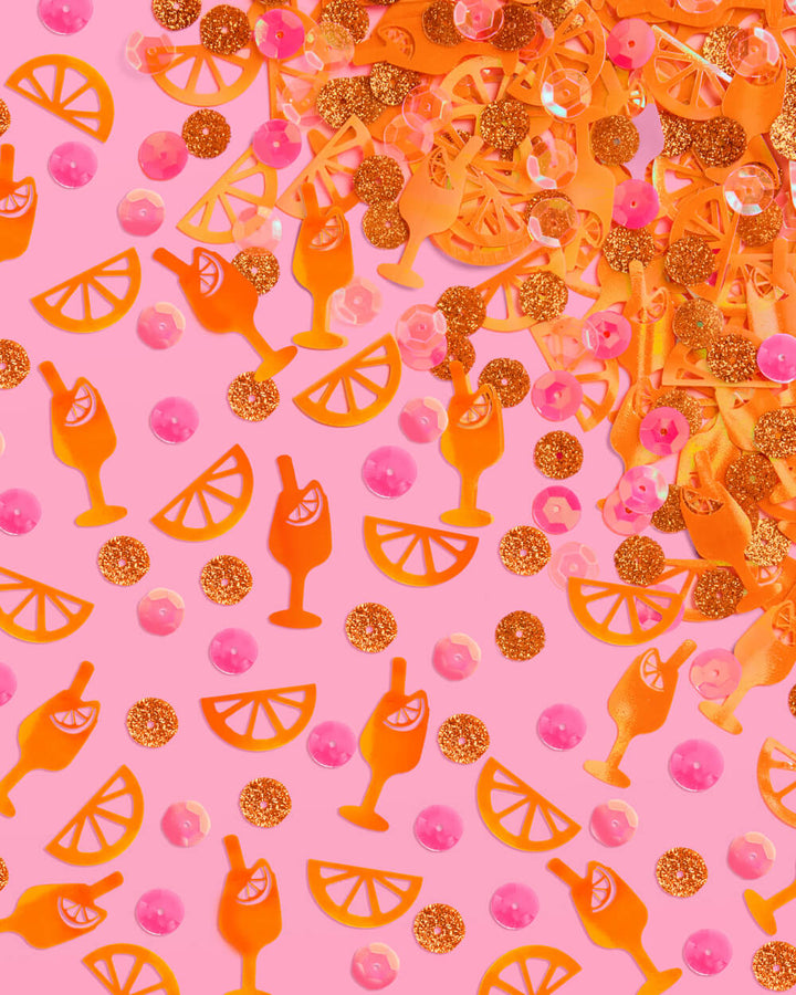 Flat lay of spritz confetti with orange cocktail glasses, citrus slices, gold glitter, and pink sequins