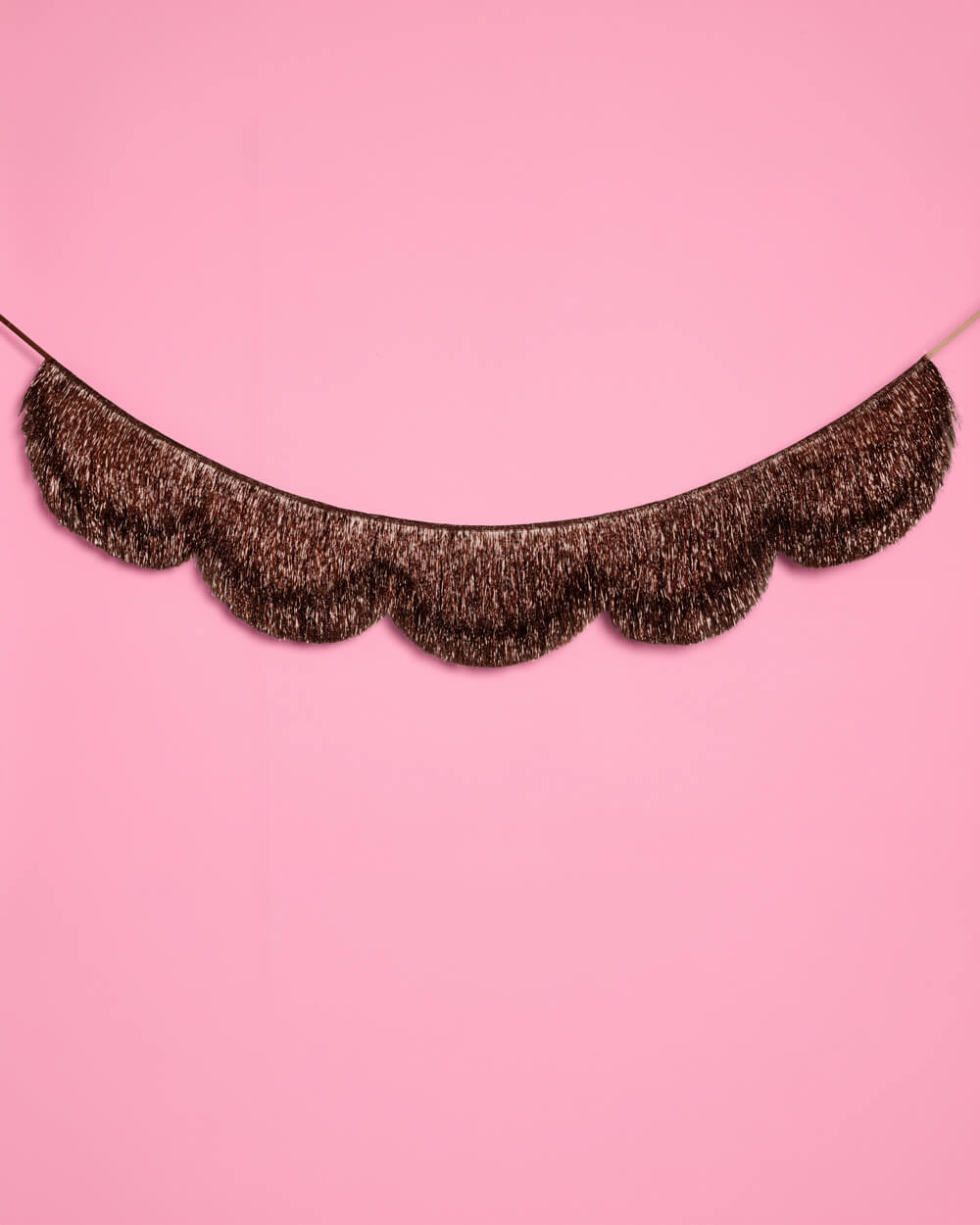 Espresso brown scalloped fringe banner curved across a pink wall as a party backdrop