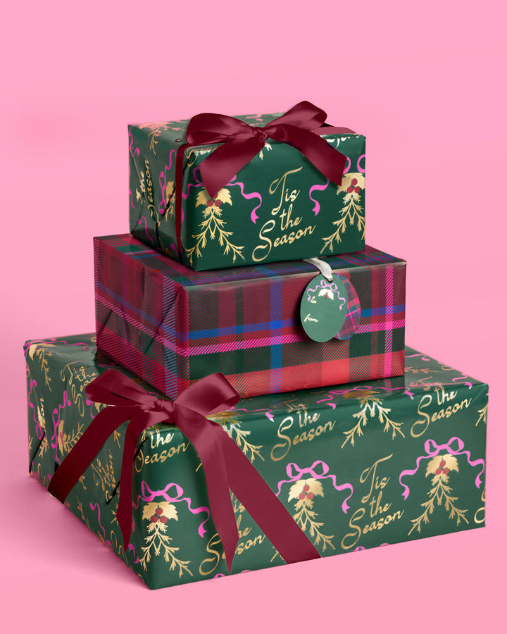 Christmas presents wrapped in deep green holly paper and tartan plaid, tied with red and green ribbon.