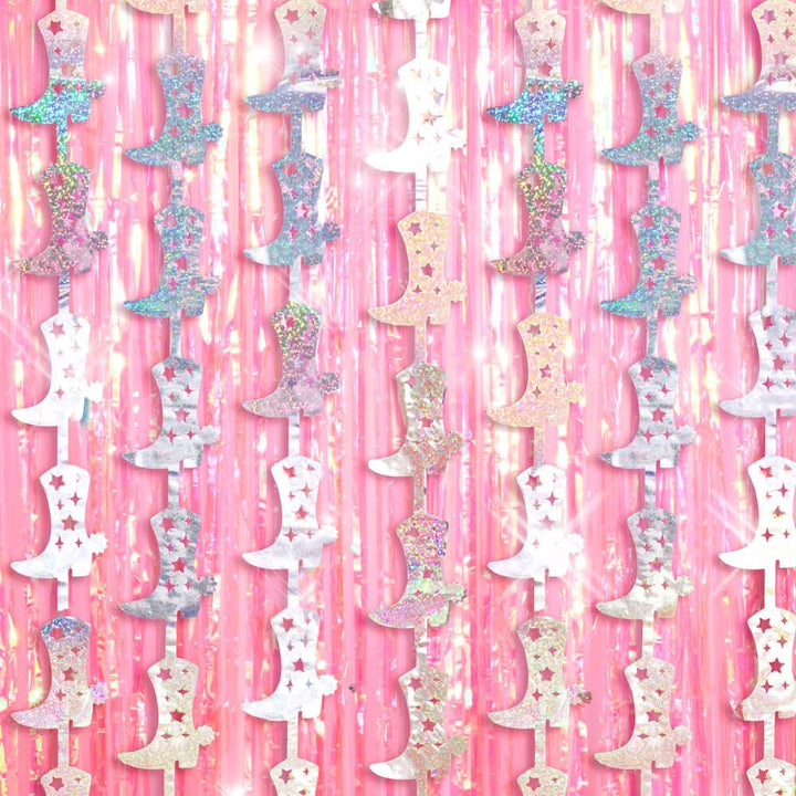 Holographic cowboy boot strands hanging over a pink foil fringe curtain for a cowgirl birthday party