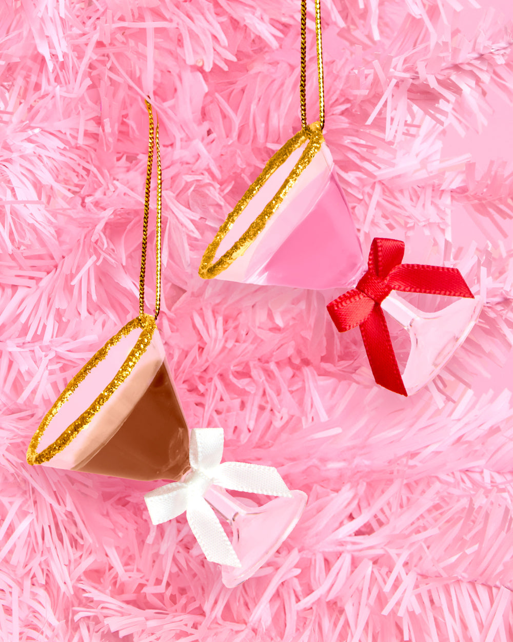 Pink martini and espresso martini ornaments with red and white bows hanging on a pink Christmas tree
