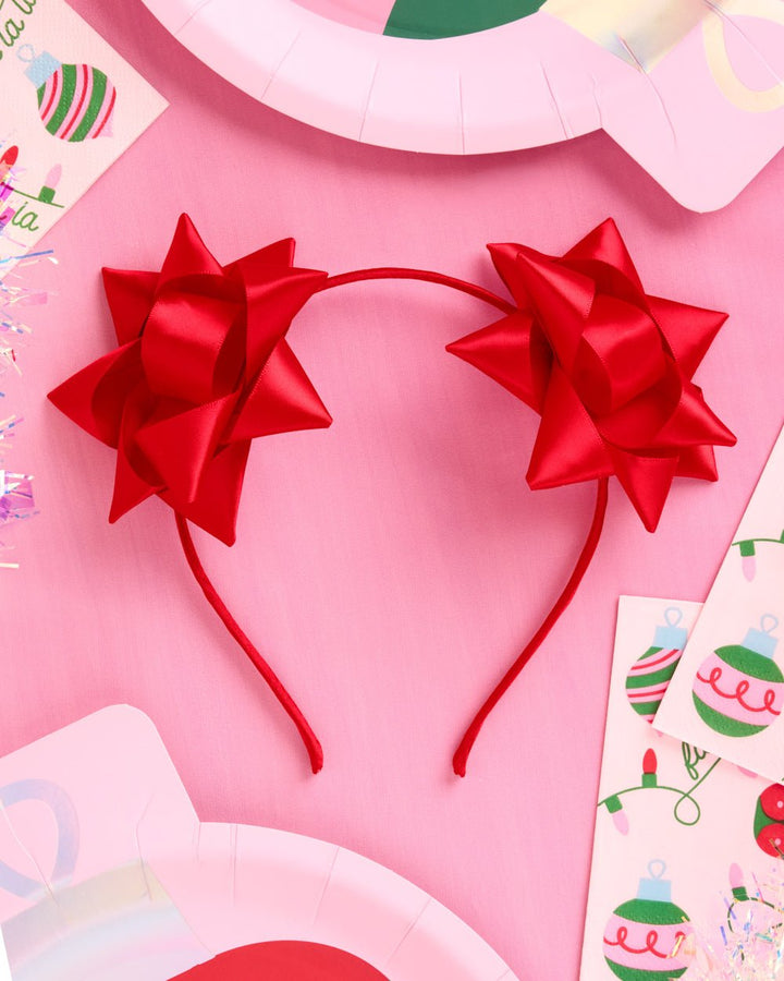 Red gift bow headband on pink with holiday paper plates and ornament print napkins