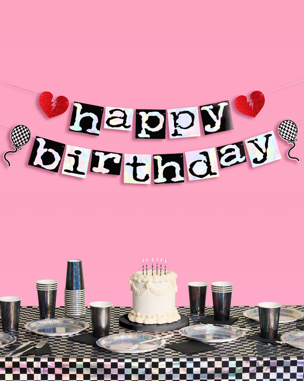 Emo happy birthday banner in iridescent foil letters on black tiles above a black checkered party table with cake
