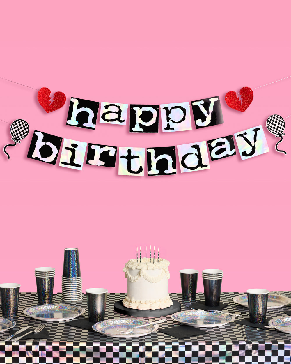 Emo happy birthday banner in iridescent foil letters on black tiles above a black checkered party table with cake
