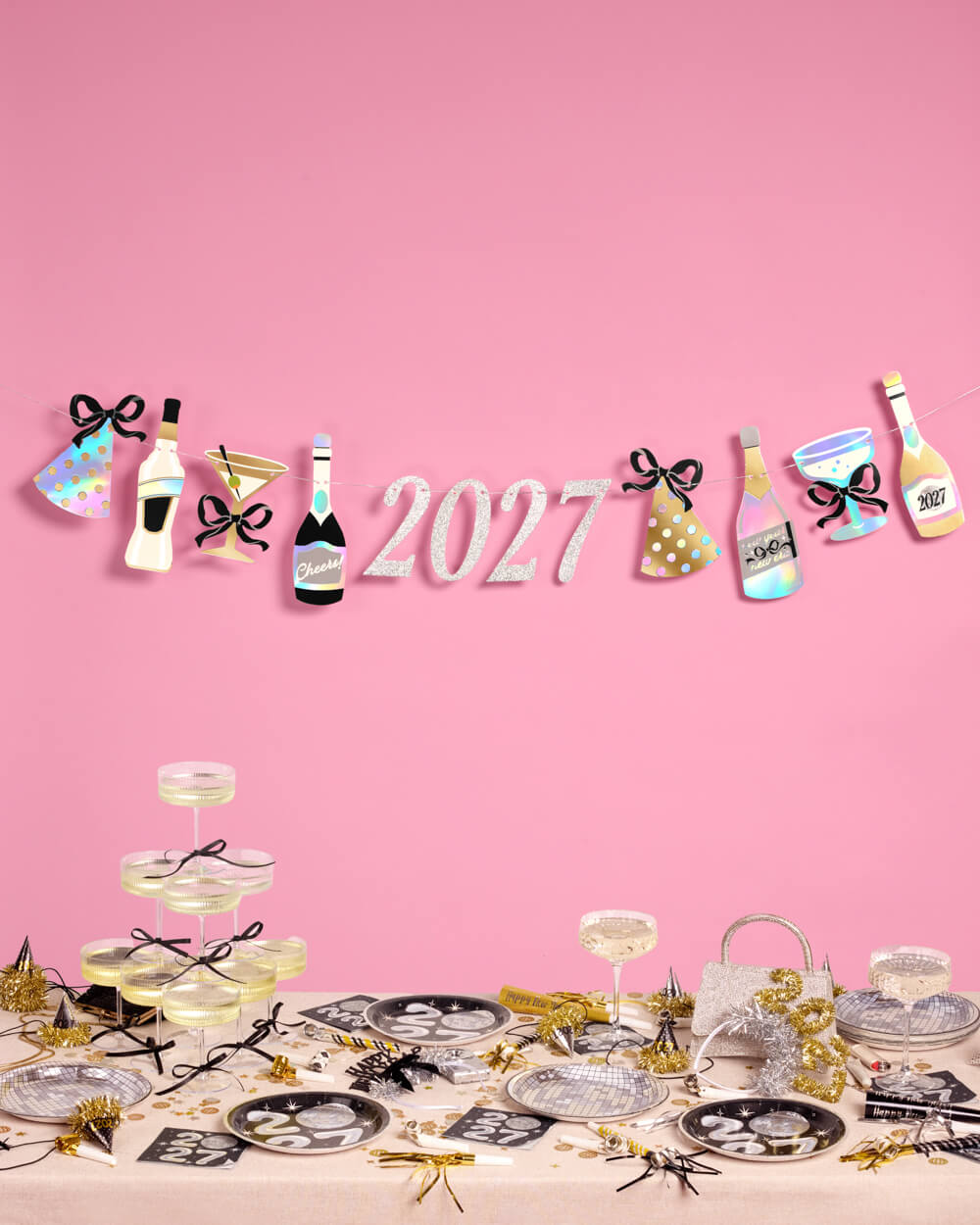 2027 New Year banner with foil bottles, cocktail glasses, and party hats above a festive table.