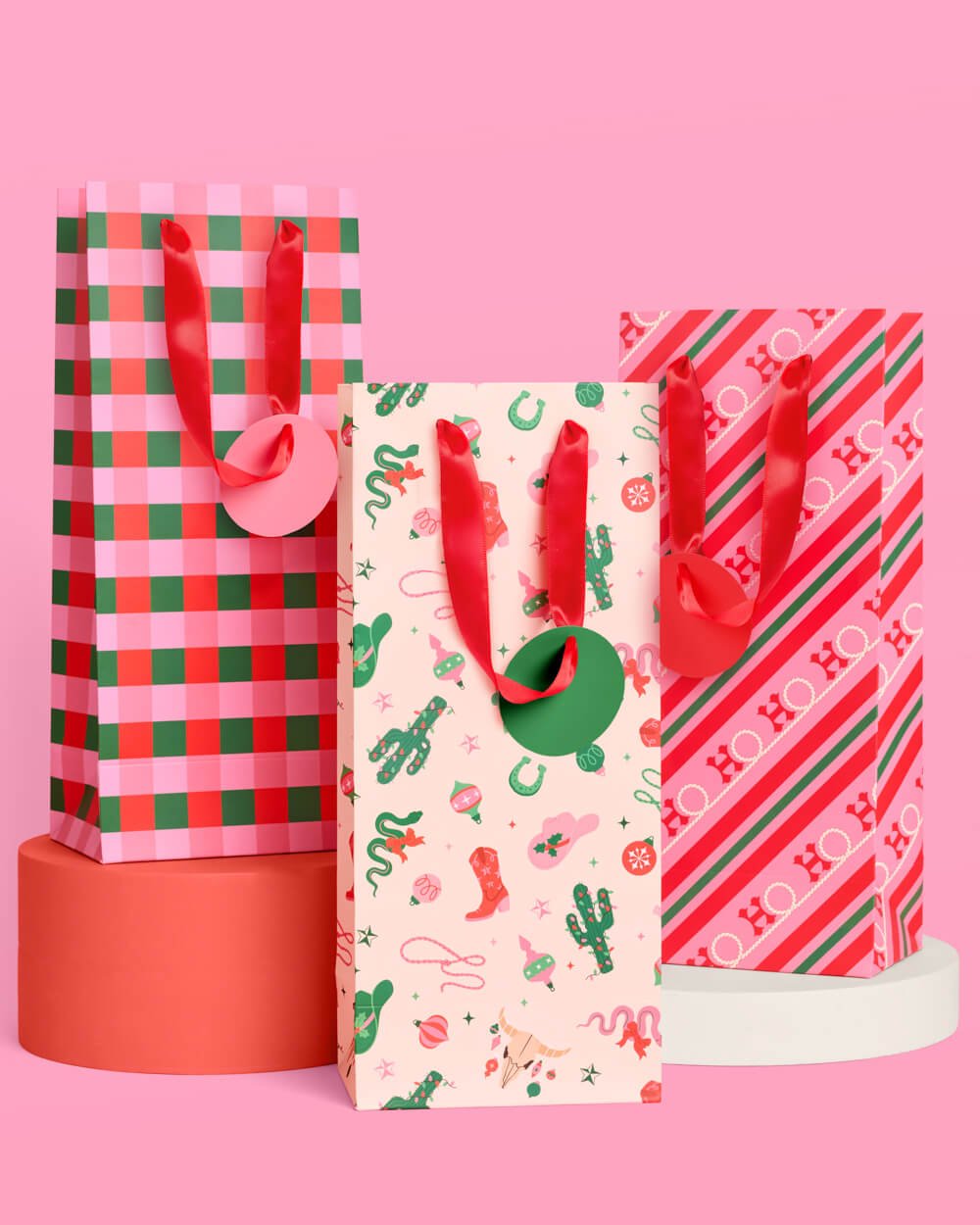 Tall western Christmas wine gift bags in gingham, cowboy print, and candy stripe, with red satin handles.