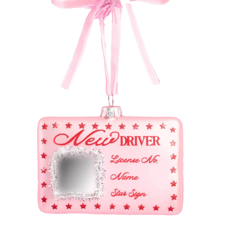 Pink driver's license-shaped glass Christmas ornament with red New Driver script, red stars, and a glittered silver photo square, hanging from a pink ribbon loop.