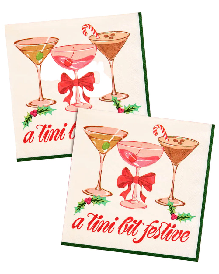 A tini bit festive Christmas cocktail napkins with three martinis, a red bow, and holly on cream paper, shown on pink