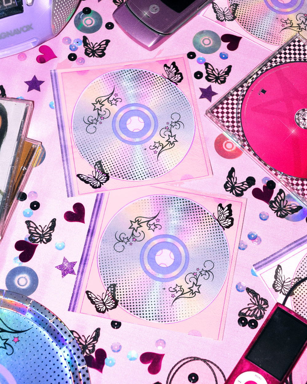 Two Y2K CD print napkins on a pink table with butterflies, hearts, stars, and a flip phone