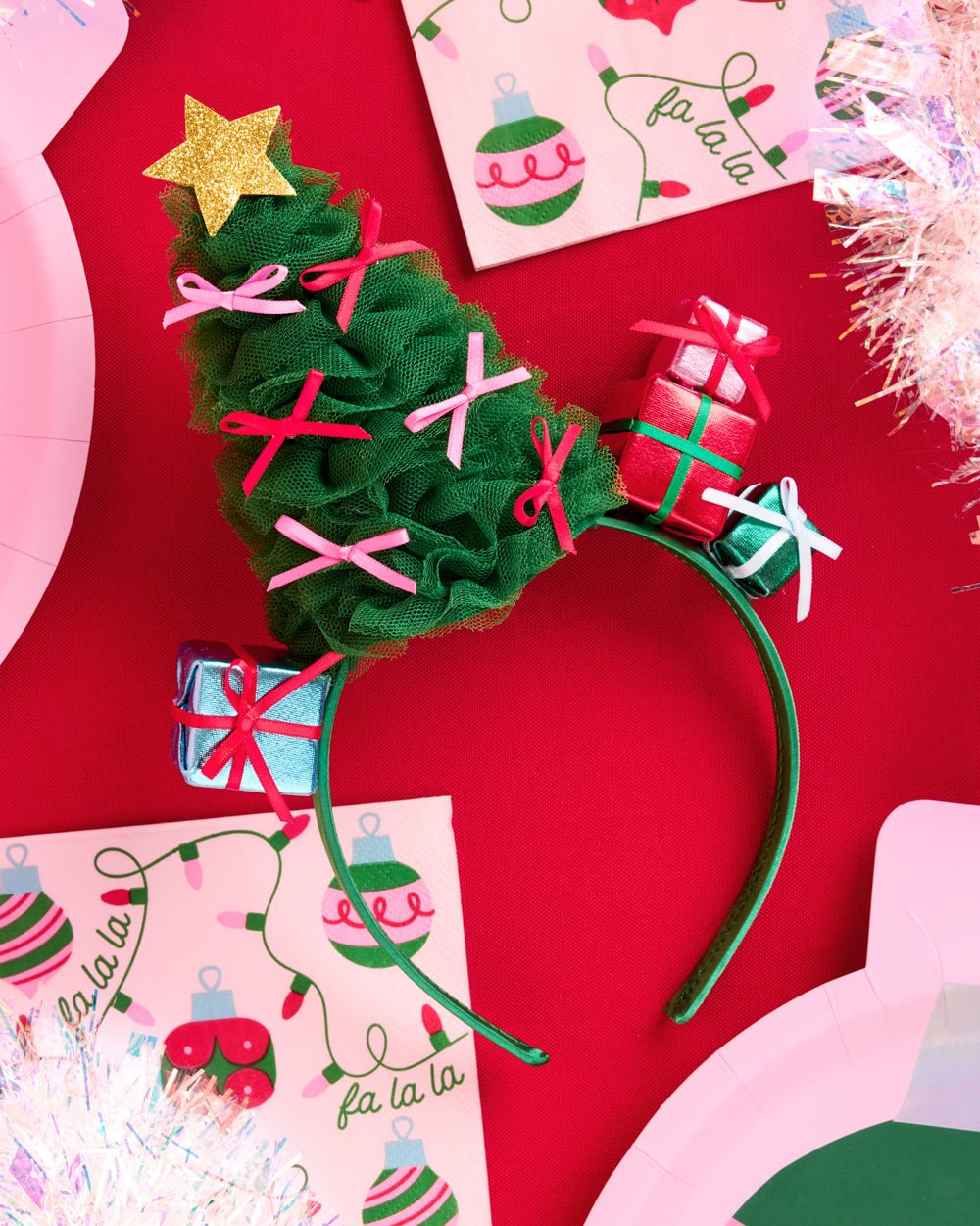 Christmas tree headband on red with fa la la napkins, pink plates, and tinsel for a Christmas party