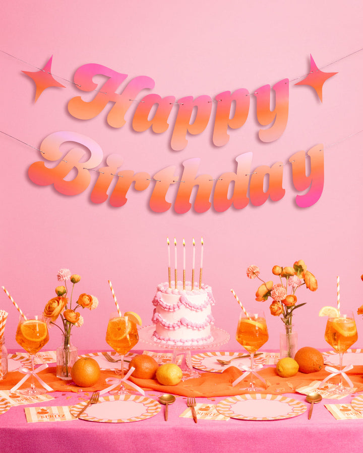 Pink and orange Happy Birthday banner with star accents hung above a birthday cake and spritz cocktail table