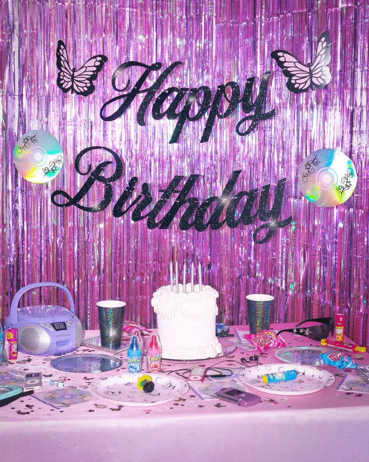Y2K birthday party bundle set up with a glitter Happy Birthday banner, plates, and confetti on a pink table