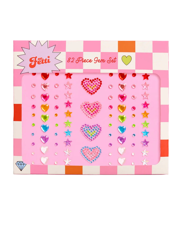 A 3D product shot of a 'Feii' brand 82-piece gem set in a pink and white checkered box. The gems are arranged in columns on a pink backing card, featuring various heart, star, and round designs in multiple vibrant colors including pink, blue, yellow, green, and purple.
