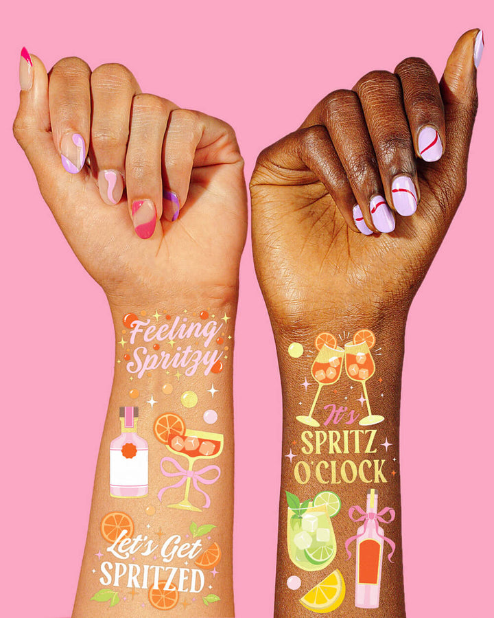 Two arms wearing spritz temporary tattoos including cocktail glasses, citrus slices, and It's Spritz O'Clock