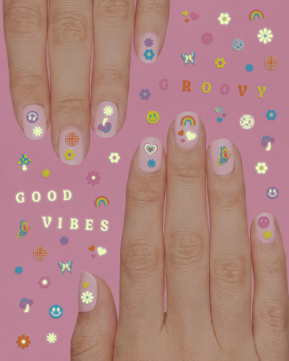 Two hands wearing groovy nail stickers with smiley faces, rainbows, and flowers on a pink sheet reading GROOVY and GOOD VIBES