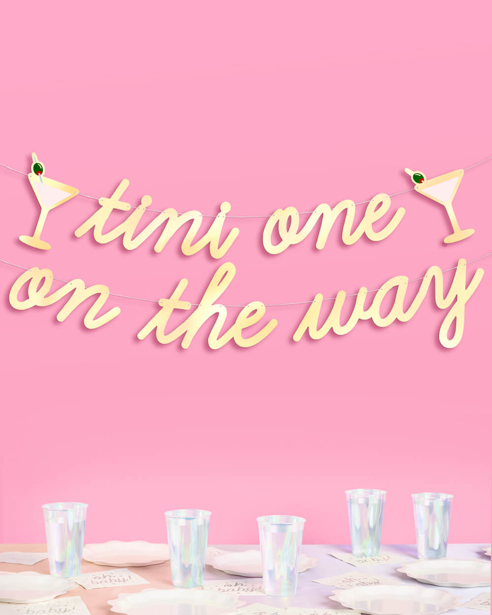 Gold foil tini one on the way baby shower banner with martini glass icons hung above a table of iridescent cups