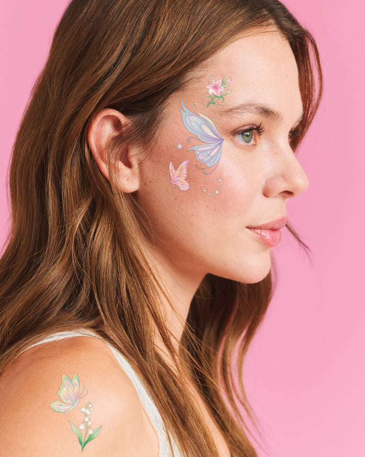 Pastel butterfly face tattoos in iridescent foil worn beside the eye and on the shoulder