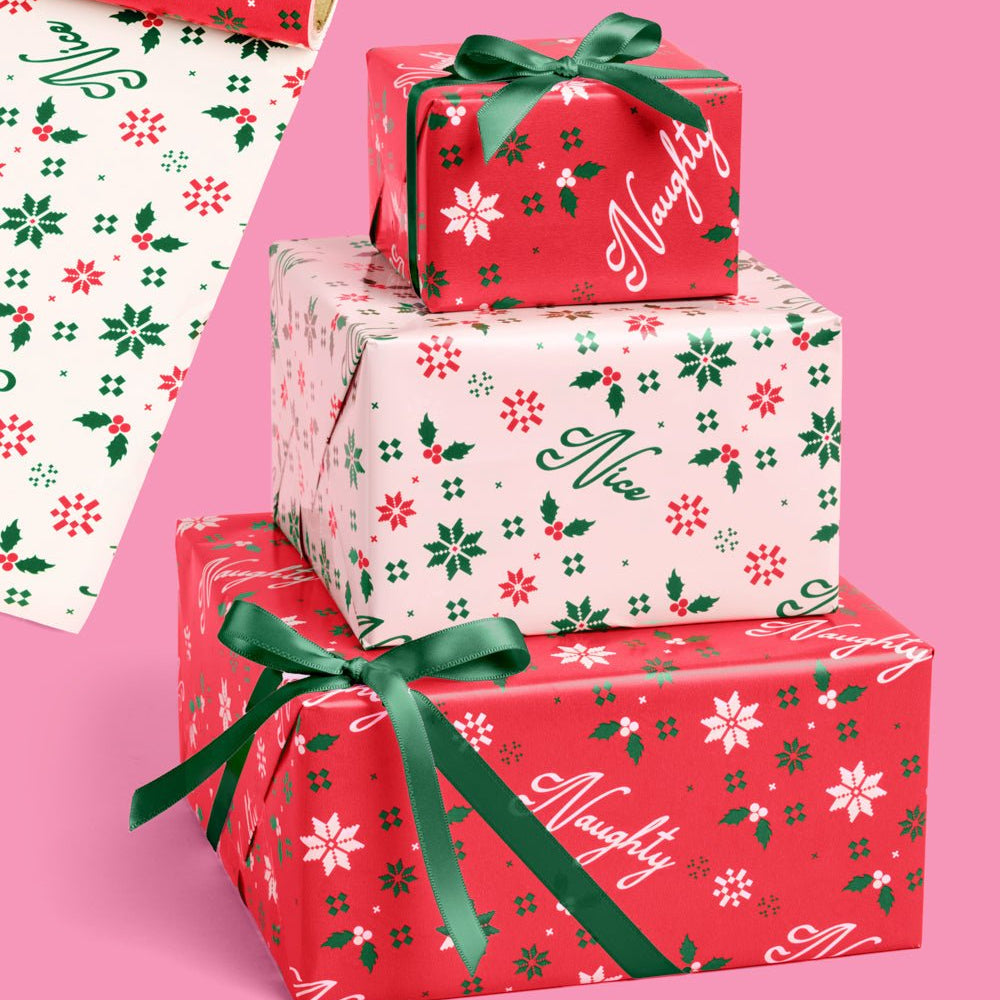 Double sided Christmas wrapping paper roll in red and cream with holly and snowflake icons, tied with green ribbon.