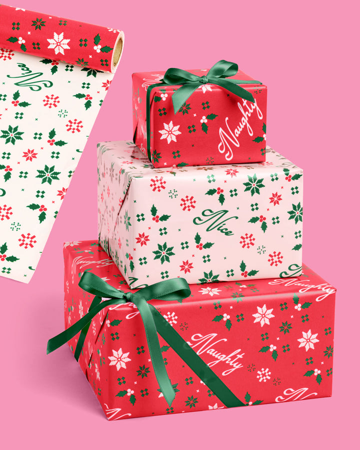 Double sided Christmas wrapping paper roll in red and cream with holly and snowflake icons, tied with green ribbon.