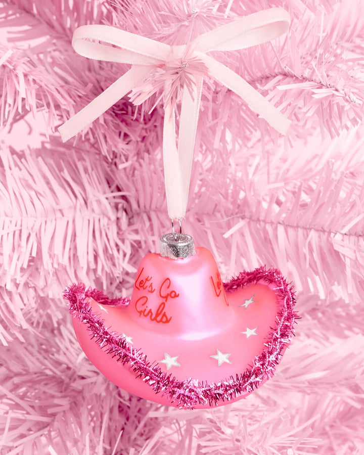Pink glass cowgirl hat ornament with pink tinsel trim and a ribbon bow hanging on a pink Christmas tree
