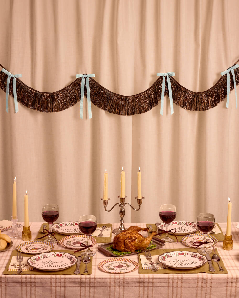Brown fringe backdrop with light blue velvet bows behind a Thanksgiving table set with a turkey, candles, and wine glasses