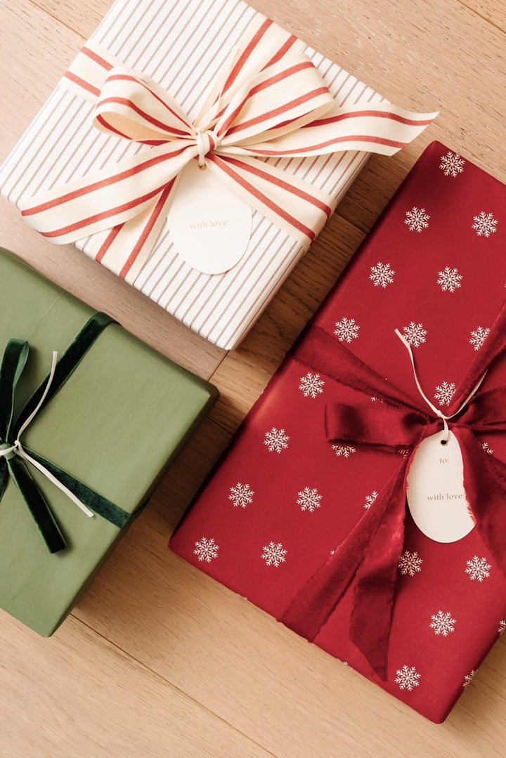 Gifts in red snowflake, cream pinstripe, and soft green paper with striped and velvet bows on wood