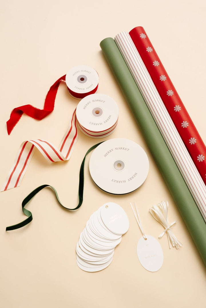 Snowflake Christmas wrapping paper kit flat lay: three rolls, velvet and striped ribbons, and oval gold foil tags