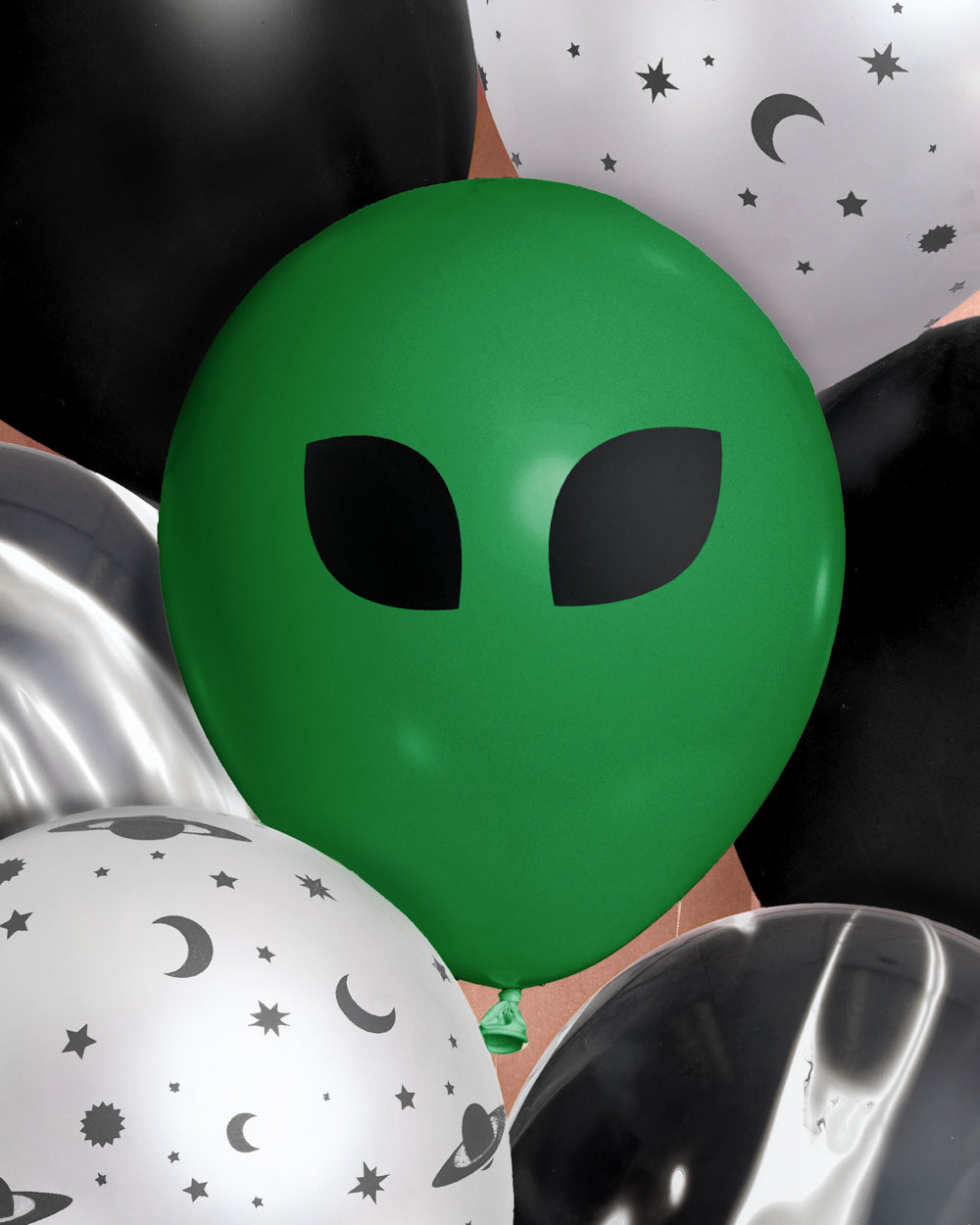 Close-up of a green alien face latex balloon among black and silver space-print balloons