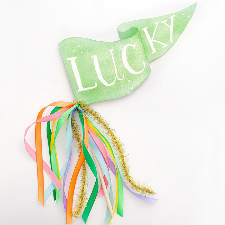 Green Lucky pennant flag with rainbow ribbons and gold tinsel on a wood dowel