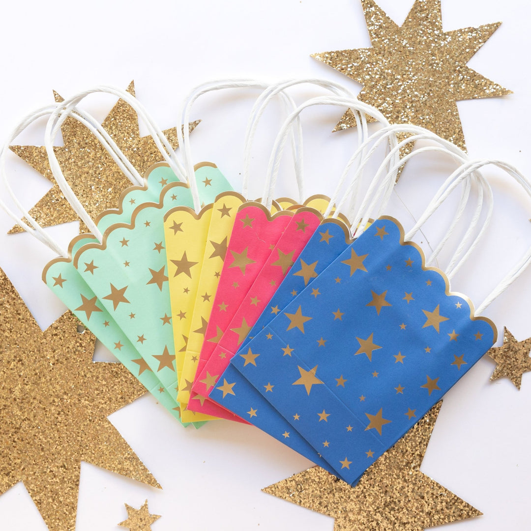Fanned row of mint, yellow, pink, and blue star print favor bags on white with glitter gold star cutouts
