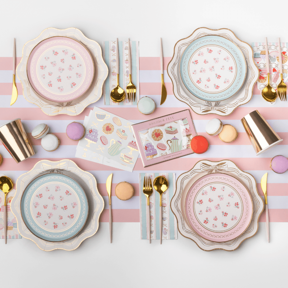 Pastel tea party table with minty blue and pink floral dessert plates, gold cutlery, macarons, and striped paper cups