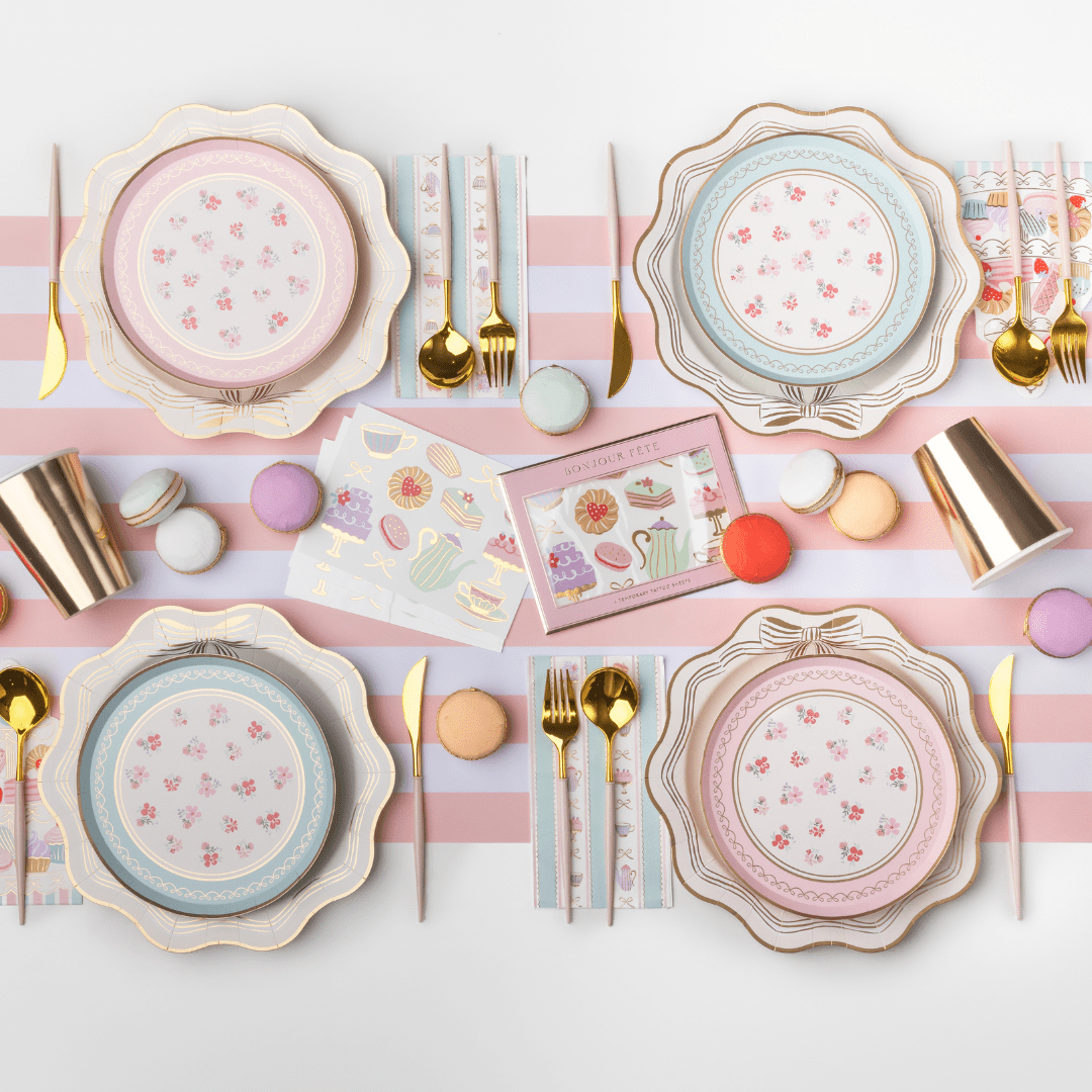 Pastel tea party table with minty blue and pink floral dessert plates, gold cutlery, macarons, and striped paper cups