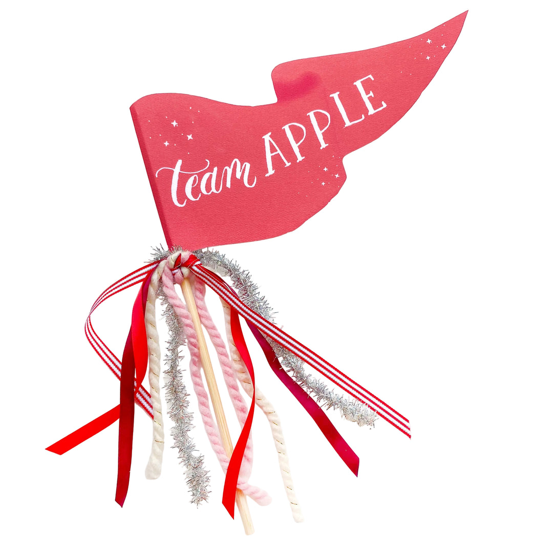 Red Team Apple party pennant with white script, striped ribbon, silver tinsel and yarn streamers on a wooden dowel