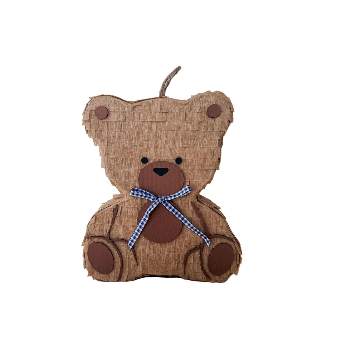 Teddy bear-shaped piñata with a blue ribbon on a beige background