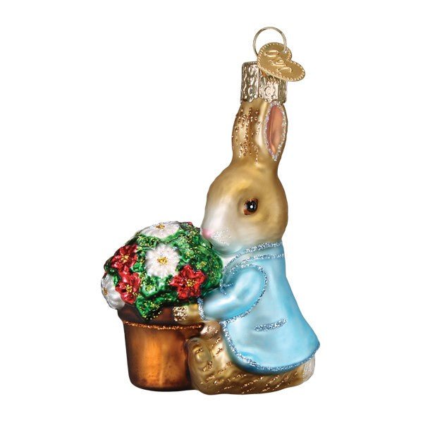 Peter Rabbit ornament in a blue jacket hugging a pot of red and white flowers, side view on white