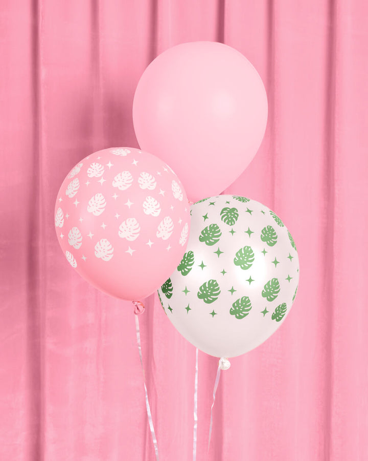 Close-up of pink and white latex balloons with a green palm leaf print