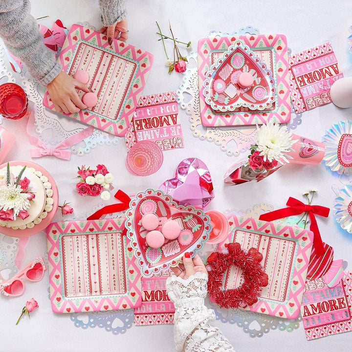 Hands arranging a Valentine's table with red velvet bows, heart trays, and a cake