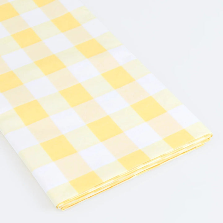 A folded piece of paper tablecover with a yellow and white gingham checkered pattern, displayed on a clean white background.