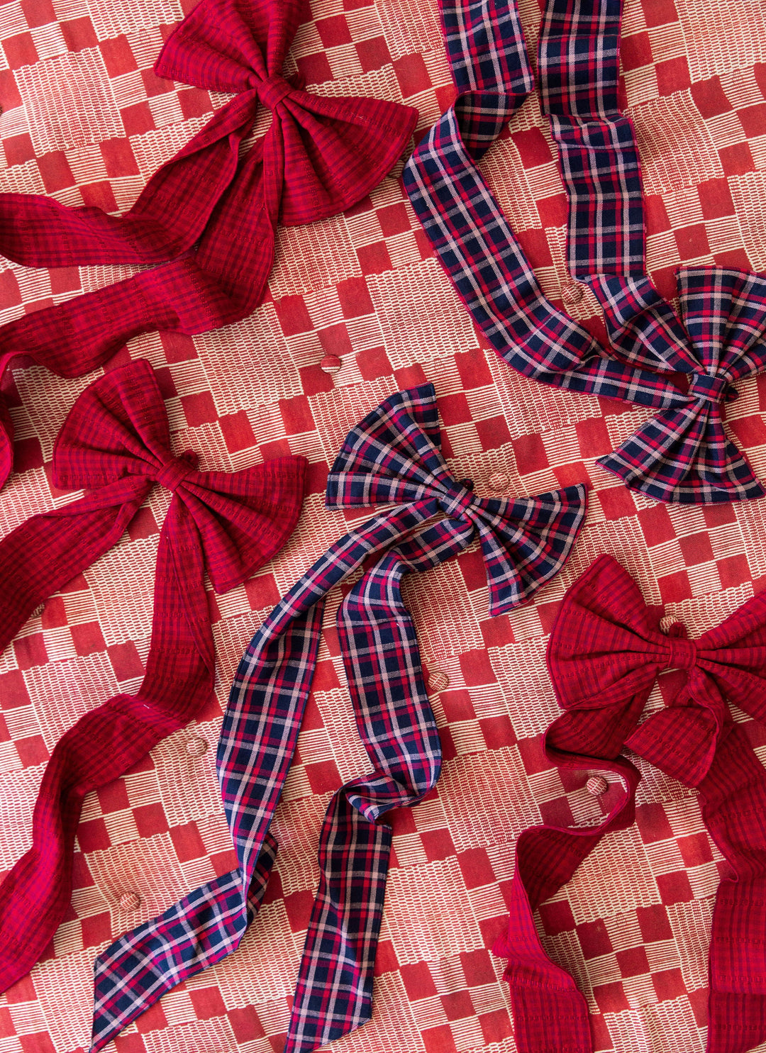 Several navy plaid and red cotton bows scattered across a pink woven tablecloth