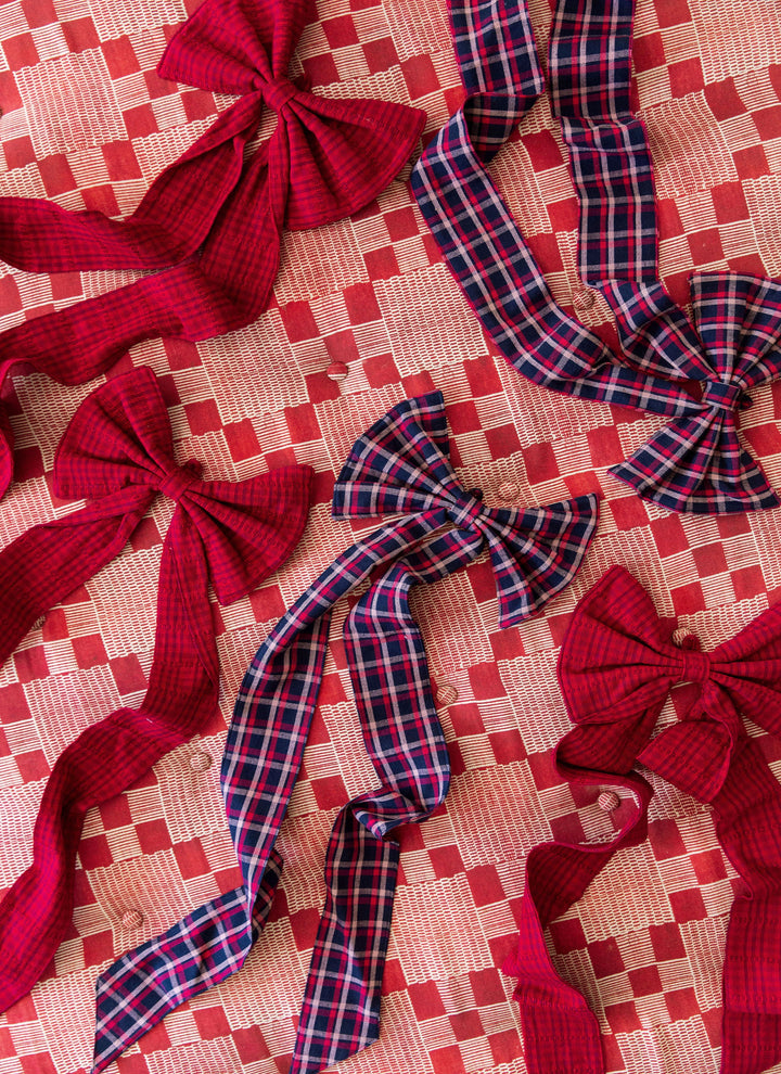 Several navy plaid and red cotton bows scattered across a pink woven tablecloth